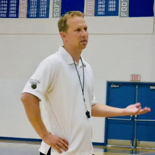 Ryan Irmer coaching in a gym, in a white polo with a whistle around his neck.
